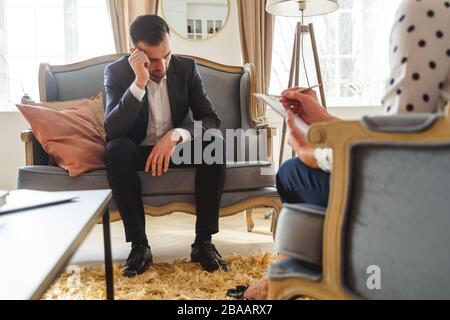 Low-spirited dark-haired man sitting on a sofa Stock Photo