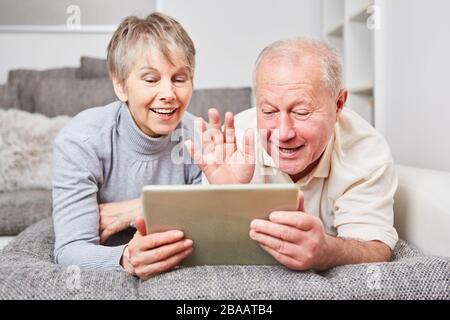 Happy senior couple having video chat with tablet computer in living room Stock Photo