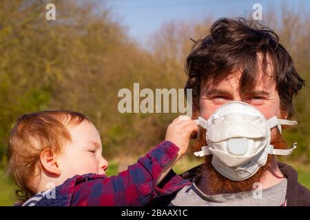 Father with facemask and baby trying to remove it Stock Photo