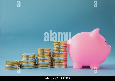 A children;s savings concept of stacks of gold and silver coins creating an upwards profit forecast towards a pink, kids piggy bank with copy space Stock Photo