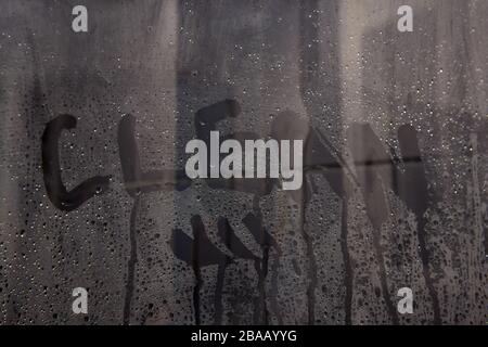 letters CLEAN on the glass. handwritten lettering written on glass with white foam on gray stuface with water drops Stock Photo