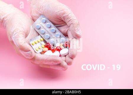 Men's hands in white rubber gloves hold many multi-colored pills on a pink background Stock Photo