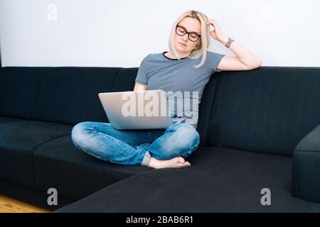 Distance online learning education and work. Female Person working office work remotely from home. Casual woman with eye glasses using laptop in huis Stock Photo