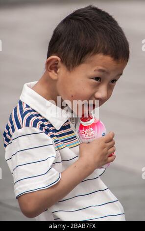 Shanghai, China - May 4, 2010: Closeup of boy child in white shirt sipping yoghurt out of red plastic bottle. Stock Photo