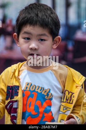 Shanghai, China - May 4, 2010: Closeup of boy wearing yellow vest and Howdy shirt looks puzzling into camera. Stock Photo