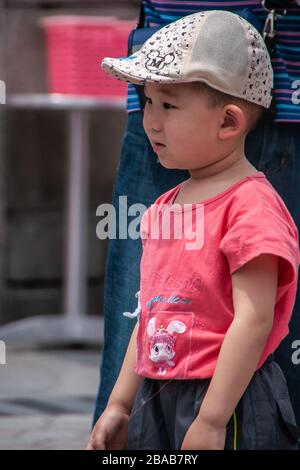 Shanghai, China - May 4, 2010: Closeup of boy wearing rose shirt and beige baseball cap, looking relaxed and observing. Stock Photo