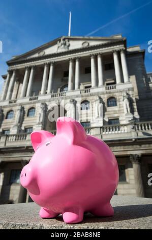 Bright pink piggy bank standing outdoors in front of the Bank of England in The City financial district of London, UK Stock Photo