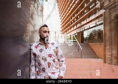 Bearded male with hand on pocket leaning on wall, looking camera Stock Photo