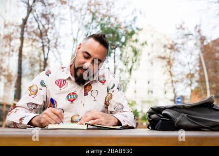 Bearded man sitting outdoors while working over a wooden table Stock Photo