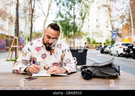 Bearded man sitting outdoors while working over a wooden table Stock Photo