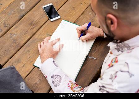 Young bearded businessman sitting at table, making notes in notebook Stock Photo