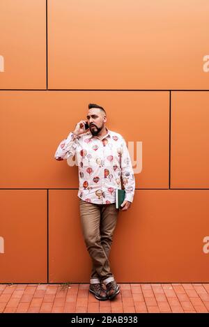 Bearded man leaning on a wall chatting on a mobile Stock Photo