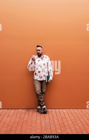 Bearded man leaning on wall while using smartphone by office building Stock Photo