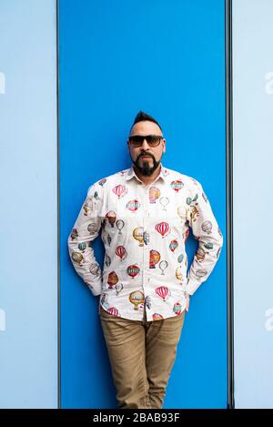 Bearded male leaning on colored wall with sunglasses, looking camera Stock Photo