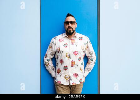 Bearded male leaning on colored wall with sunglasses, looking camera Stock Photo