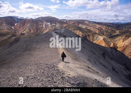 Man with cape walking down trail on top of mountain in Iceland Stock Photo