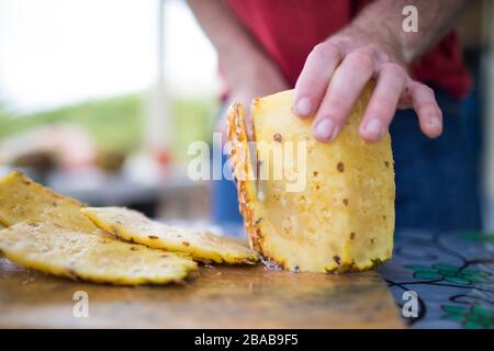 Detailed view of man slicing fresh pineapple outdoors Stock Photo