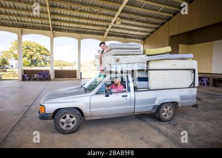 Two men riding on loaded truck help to move mattresses at orphanage. Stock Photo