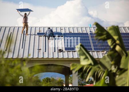 Two men install sustainable solar panels in rows on roof top. Stock Photo