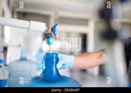 Worker holds top of water jug while filling it with drinking water. Stock Photo