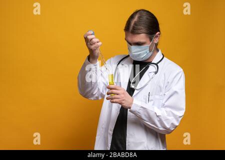 Young doctor using a pipette and a yellow tube, wearing protection mask and a stethoscope is trying to find a vaccine against sars-cov-2 virus pandemy Stock Photo