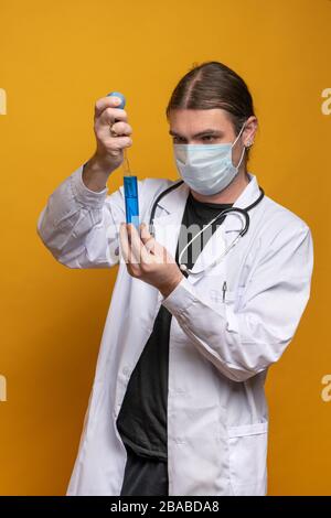Young doctor using a pipette and a blue tube, wearing protection mask and a stethoscope is trying to find a vaccine against sars-cov-2 virus pandemy i Stock Photo