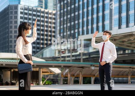 Asian business man and woman greet and say hello with business colleague and wearing mask standing distance of 1 meter distance protect from COVID-19 Stock Photo