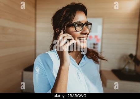 Smiling businessman talking on phone. Female executive standing in office making a phone call. Stock Photo