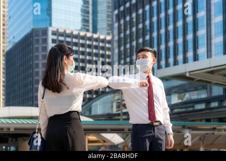 Elbow bump is new novel greeting to avoid the spread of coronavirus. Two Asian business friends meet in front of office building. Instead of greeting
