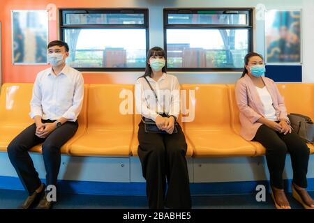 Three Asian people wearing mask sitting in subway distance for one seat from other people keep distance protect from COVID-19 viruses and people socia Stock Photo