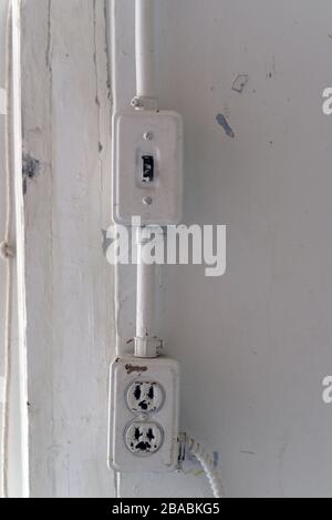 An old and worn light switch and an electrical plug on a painted white wall Stock Photo