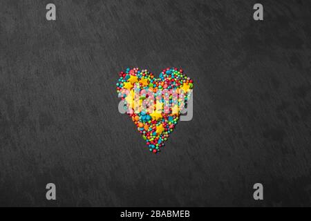 Sprinkle heart shape background. Sprinkle in the form of stripes, balls, stars on a black background. copy space. concept of an Easter plan. top view photo Stock Photo