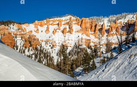 After a new storm brings in lots of snow, the sun shines on a clear day in Southern Utah. Red rock formations and cliffs surrounded by winter snow in Stock Photo