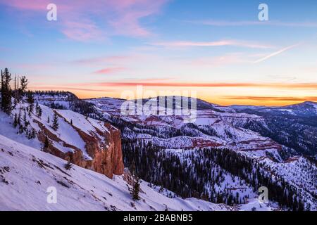Pink and orange colorful clouds overhead at sunset. Below, orange and red rock covered in snow in Southern Utah winter scene. Stock Photo