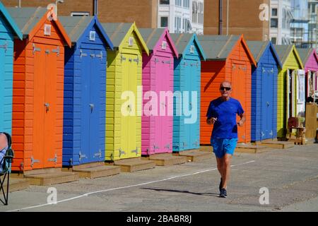 Older man jogging along a seafront by colourful beach huts. Seaford, UK Stock Photo