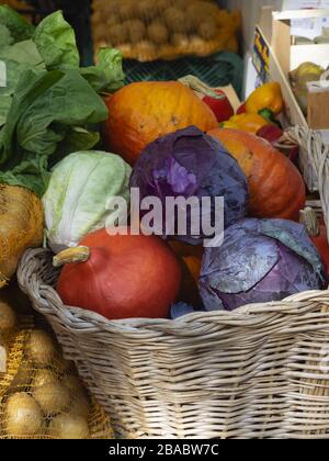 wicker basket full of colorful pumpkins and cabbage for sale with other vegetables in a country market Stock Photo