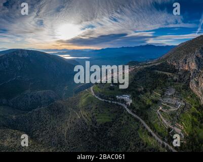 Aerial view of Delphi, Greece, the Gulf of Corinth, orange color of clouds, mountainside with layered hills beyond with rooftops in foreground Stock Photo