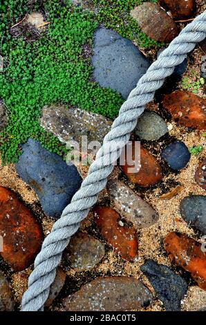 old colorful cobble stones and low lying weeds with blue boat rope Stock Photo