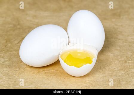 chicken white eggs with half broken egg on beige textured background Stock Photo