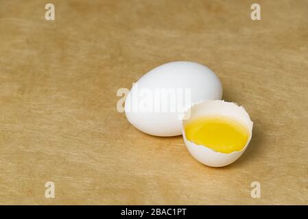 chicken white eggs with half broken egg on beige textured background Stock Photo