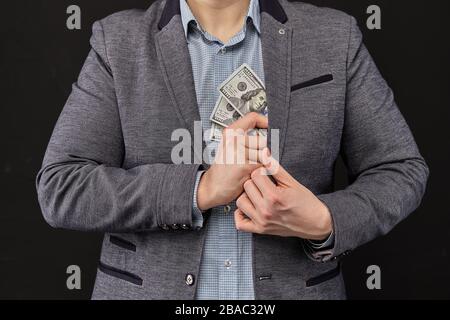 A man in a jacket removes us dollars in a jacket on a black background. Close up. Stock Photo