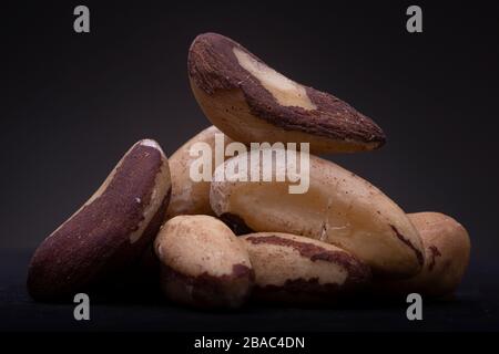 Closeup macro shot of a pile of partly peeled from its nutshell Brazil nuts low key still life contrasted against a dark grey background Stock Photo