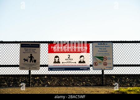 White Rock, Canada - March 25, 2020: Social Distancing notice and general signs affixed to fence on public Promenade walkway Stock Photo