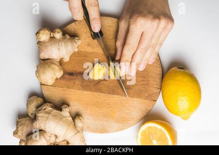 Overhead shot of a person cutting ginger roots next to lemons on a wooden board Stock Photo