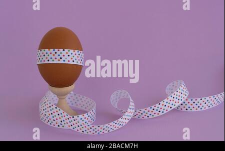 Egg standing on cup, on a soft purple background. Easter egg tied with a festive ribbon Stock Photo