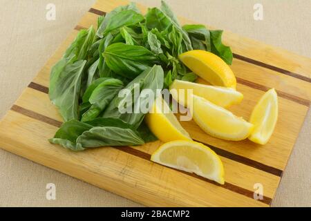 Fresh ingredients of raw yellow lemon wedges and fresh basil leaves on wooden cutting board Stock Photo
