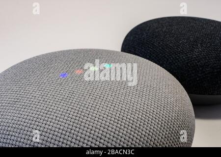 A close-up view of a Google Nest Mini smart speaker shows its colored lights activated, with another Nest Mini sitting behind it. Stock Photo