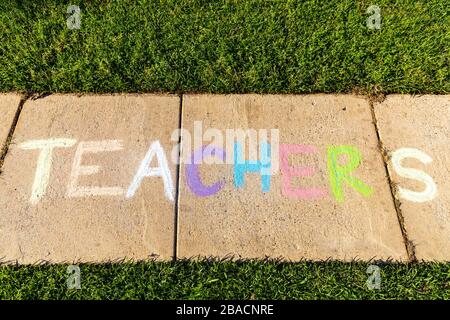 The word "Teachers" written with sidewalk chalk, on gray concrete pavement background. Stock Photo