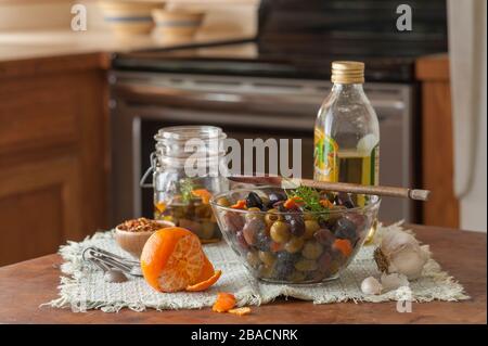 Preparing olive oil marinated black and green olives with spices in kitchen. Stock Photo