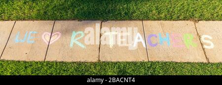 The words "We Love Our Teachers" written with sidewalk chalk, on gray concrete pavement background. Stock Photo